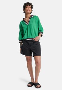 Pull-over vert en tricot avec un col rayé noir et blanc, accompagné d'un short en denim noir et de sandales noires ; coupe décontractée et manches courtes.