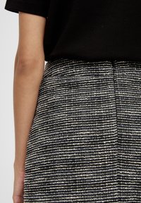 Detailní záběr na pas osoby, která nosí černý top a strukturovanou sukni s černobílými pruhy a bočním zipem.