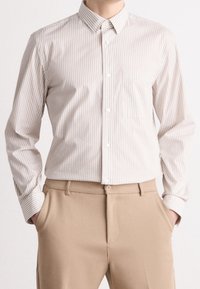 Vaaleabeige nappipaita, jossa pystysuorat kermaiset raidat, pitkät hihat ja rintatasku. Yhdistetty beežin värisiin housuihin, joissa on sileä pinta.