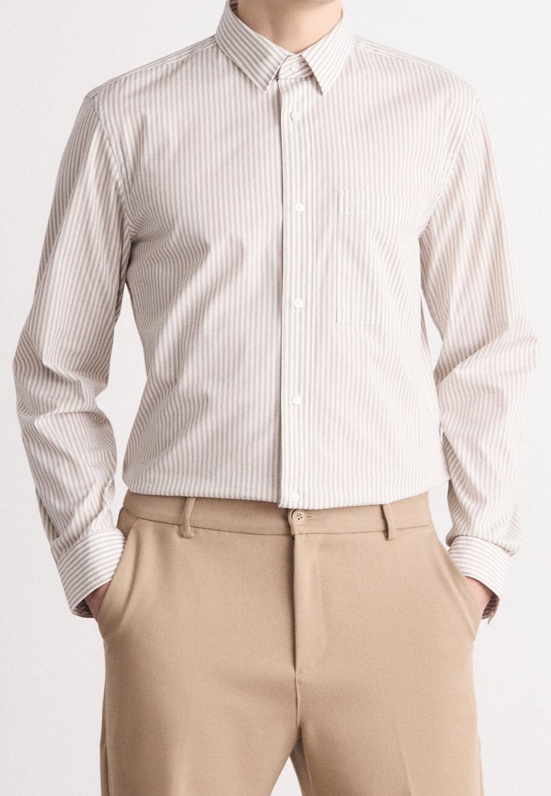 Vaaleabeige nappipaita, jossa pystysuorat kermaiset raidat, pitkät hihat ja rintatasku. Yhdistetty beežin värisiin housuihin, joissa on sileä pinta.