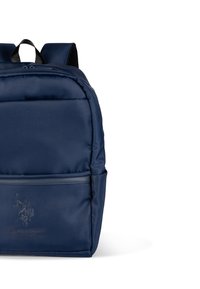 Zaino blu navy realizzato in tessuto liscio, con una tasca frontale con cerniera e un logo in rilievo. Spallacci imbottiti e maniglia superiore per il trasporto.