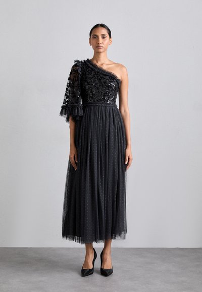 Black one-shoulder dress with embroidered sequins and sheer ruffle sleeve, tulle skirt features polka dot pattern, ankle-length, paired with heels.