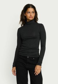 Dark gray turtleneck top with long sleeves, made from a soft, fitted material. Smooth texture and subtle gathering at the waist.