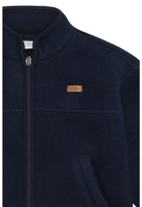 Marineblaue Fleecejacke mit hohem Kragen, vorderem Reißverschluss und einem kleinen hellbraunen Lederlabel. Verfügt über seitliche Taschen und eine glatte Textur.