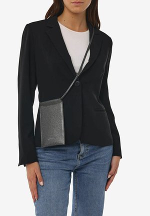 Sort blazer over en hvid top, parret med klassiske blå jeans. En lille, struktureret sølv crossbody taske hænger fra en tynd rem.