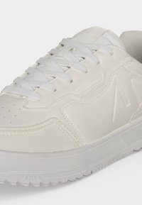 Άσπρο χαμηλό sneaker με παχιά σόλα, υφασμένη εξωτερική σόλα, ραμμένες λεπτομέρειες και άσπρα υφαντά κορδόνια περασμένα από οπές.