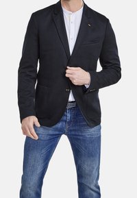Granatowy blezer z dwoma przednimi kieszeniami, zapięciem na jeden guzik i klapami, noszony z białą koszulą i dżinsami.