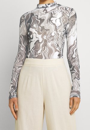 Top de manga larga y cuello alto con patrón abstracto de remolinos grises y blancos combinado con pantalones crema de talle alto y pierna ancha.