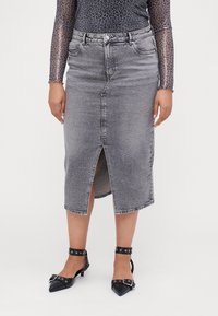 Gonna di denim grigia a lunghezza ginocchio con uno spacco frontale, texture leggermente scolorita e un design classico a cinque tasche, abbinata a tacchi a punta neri.