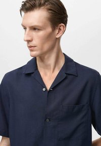 Marineblauw kortemouwen overhemd van een lichte stof. Heeft een notch-kraag, een borstzakje en een enkele knoopsluiting.