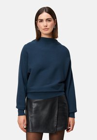 Granatowy sweter w prążki z wysokim kołnierzem, opadającymi ramionami i długimi rękawami, zestawiony z czarną skórzaną mini spódnicą.