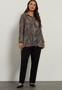 Blusa a maniche lunghe stampata in tonalità scure con motivi astratti più chiari, abbinata a pantaloni neri e scarpe basse. Tessuto morbido, vestibilità rilassata.