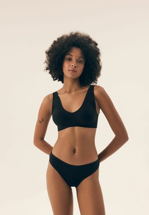 Czarny bezprzewodowy stanik typu bralette z szerokimi ramiączkami i głębokim dekoltem w kształcie litery V, w komplecie z pasującymi majtkami w stylu bikini. Gładki, elastyczny materiał.