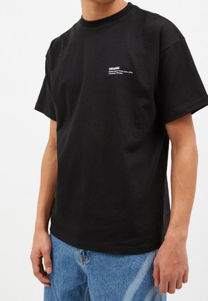 T-shirt noir à manches courtes en coton, avec un logo blanc sur la poitrine. La coupe est décontractée avec un col rond.