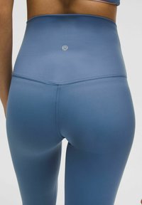 Magas derűkék leggings sima, rugalmas anyagból. A derékpánton egy kis logó található, és a hátsó részen varrási díszítés jellemzi.