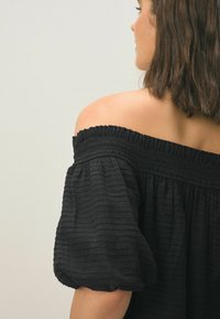 Zwarte off-shoulder top van textuurstof met kreukels. Heeft een elastische halslijn en pofmouwen, wat zorgt voor een losse pasvorm.