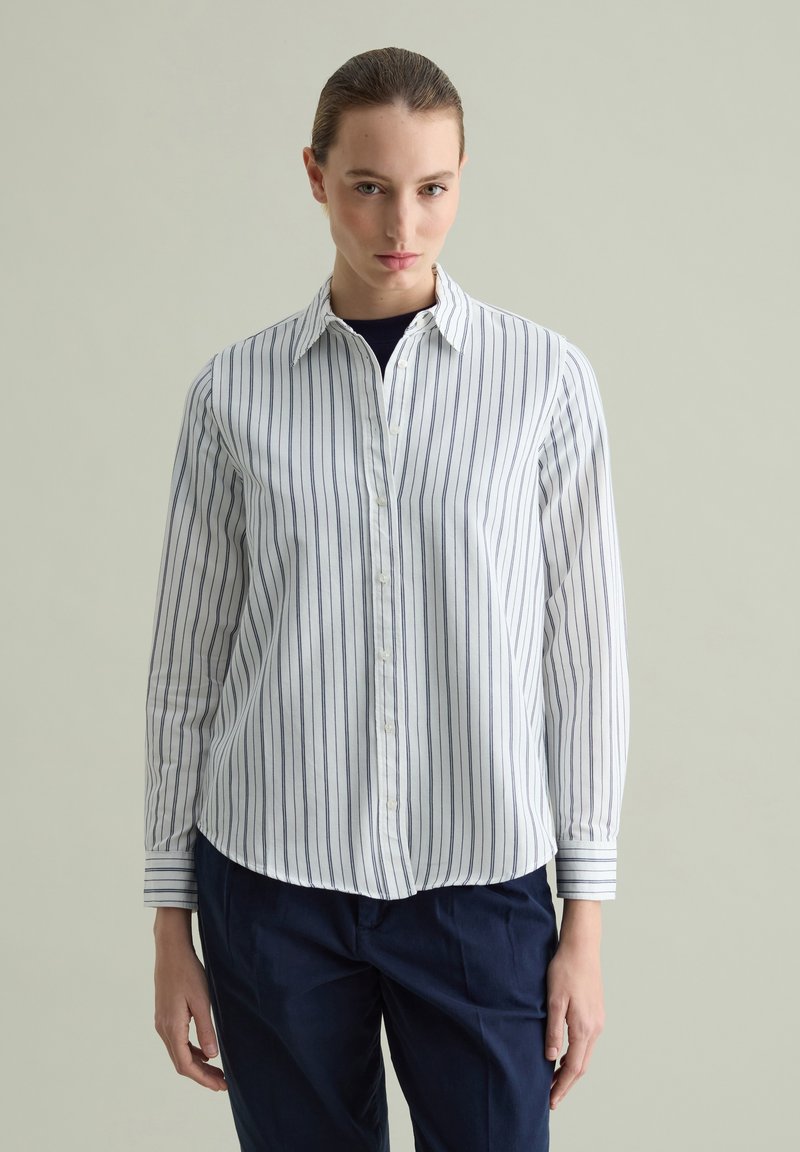 Camicia bianca con righe verticali blu navy. Presenta un colletto classico e maniche lunghe con polsini a righe. Tessuto di cotone morbido.