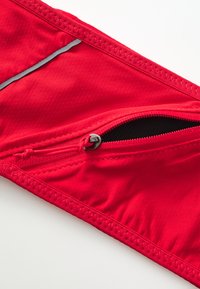 Red swim brief with textured fabric, featuring a side zipper pocket and reflective strip. Stitching is visible along the edges.