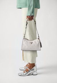 Borsa a tracolla bianca con texture, caratterizzata da un motivo imbossato e accessori in argento, abbinata a un top verde menta, pantaloni beige e scarpe metalliche argento.