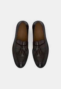 Mocassins en cuir marron à bout rond, ornés d'un pompon décoratif à l'avant et d'une semelle en caoutchouc noire contrastante. Texture lisse.