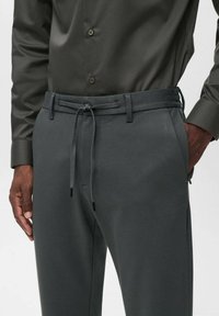 Donkergrijze broek met een gestructureerde afwerking, voorzien van een trekkoord bij de taille, riemlussen en zijzakken. Gemaakt om te dragen met een bijpassend shirt.