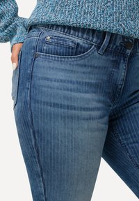 Jeans de mezclilla en diferentes tonos de azul con un patrón de rayas verticales, que presentan bolsillos tradicionales y una cinturilla ajustada.