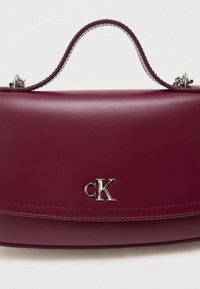 Burgundi värvi nahk käekott, millel on ülemine käepide ja hõbedane "cK" logo esiküljel, millel on hõbedased ahelad kinnituseks.