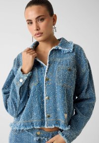 Blauwe geaderde denimjas met rafelige randen en twee voorzakken, voorzien van goudkleurige knopen en een kraagontwerp.