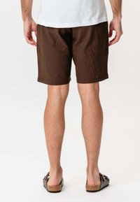 Brune bomuldsshorts med en afslappet pasform, der har sidelommer og en kantet finish. Kombineret med brune sandaler og en hvid t-shirt.
