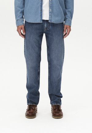 Lichtblauwe denim jeans met een recht gesneden ontwerp, gecombineerd met bruine veterschoenen met een getextureerde zool. Witte shirt eronder.