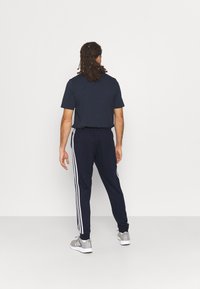 Marinblå träningströja med kort ärm och smalnande byxor med tre vita ränder på sidorna, tillsammans med grå sneakers.