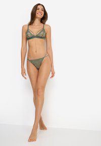 Σετ πράσινο δαντελωτό σουτιέν bralette και στρινγκ με λουλουδένια σχέδια, ρυθμιζόμενες τιράντες και τριγωνικό σχέδιο. Μαλακό, διαφανές υλικό με λεπτές λεπτομέρειες.