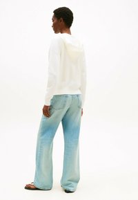 Witte hoodie met een capuchon, gecombineerd met lichtblauwe wijde jeans. De jeans hebben een vervaagde wassing en subtiele details op de achterzakken.