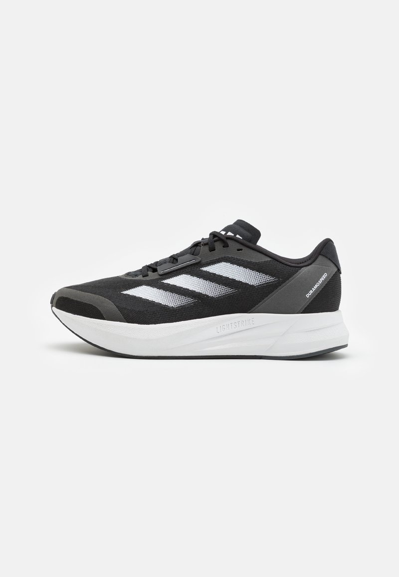 Scarpe da ginnastica nere con una tomaia in rete testurizzata, tre strisce bianche, una suola bianca imbottita e una punta rinforzata.