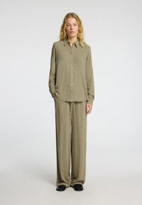 Chemise à manches longues en olive léger et boutonnée, associée à un pantalon ample assorti. Design simple avec une silhouette droite et une texture douce.