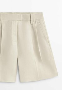 Short beige taille haute avec plis à l’avant, poches latérales, fermeture avant dissimulée et deux passants de ceinture boutonnés à la taille.