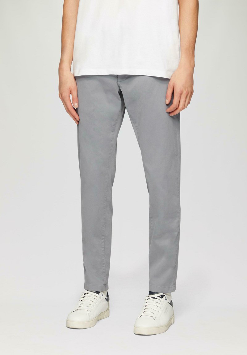 Sivé bavlnené chinos nohavice so slim fit strihom, s plochým predným dielom a bočnými vreckami, doladené s bielymi teniskami a jednoduchým bielym tričkom.