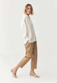 Bílá košile na knoflíky, béžové tailored kalhoty a tělové slingback podpatky. Hladká tkanina, volný střih a jemné detaily zvýrazňují design.