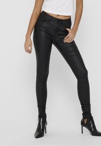 Pantaloni aderenti in ecopelle nera con una texture liscia e lucida e una silhouette aderente, abbinati a stivaletti neri a punta.