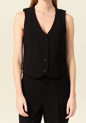 Sleeveless black buttoned vest worn over matching black pants on a person with light skin and long hair.