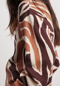 Stickad tröja i jordnära toner av brunt, beige och rost. Har ett vågigt abstrakt mönster och en texturerad yta på tyget.