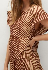 Robe rayée brun et beige avec des manches courtes, taille froncée et jupe fluide. Fabriquée en tissu léger avec une texture douce.