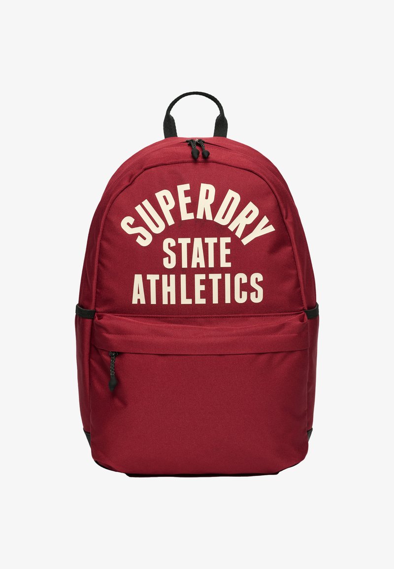 Mochila roja con asa y cremallera negra, bolsillo frontal y texto en blanco en negrita "SUPERDRY STATE ATHLETICS" en el compartimento principal.