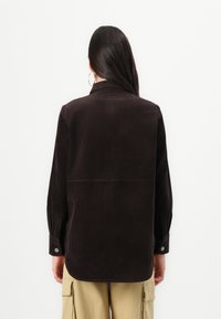 Brown corduroy shirt with a structured collar, buttoned cuffs, and a back yoke detail, worn with khaki cargo pants.