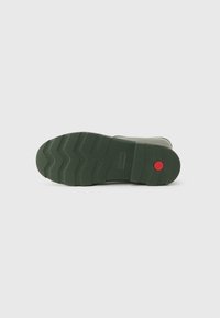Rubber boot sole in dark green with a textured surface, featuring zigzag patterns for grip and a red circular accent on the heel.