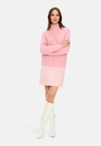Rosa gerippter Strickpullover mit hohem Kragen, kombiniert mit einem hellrosa Rock und weißen kniehohen Stiefeln mit strukturierten Details.