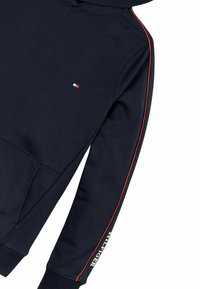 Felpa con cappuccio blu navy caratterizzata da strisce laterali rosse, un piccolo logo sul petto e polsini a coste. Il materiale ha una texture liscia.