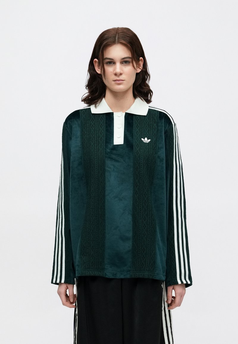 Green velour long-sleeve polo with a white collar, three buttons, and an embroidered logo. Features white stripes on sleeves and intricate patterns.