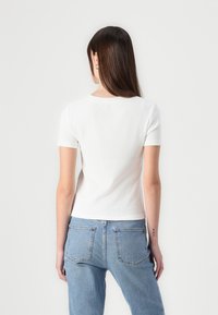 Tricou alb, cu maneci scurte, din material texturat, cu guler rotund, asociat cu blugi din denim deschis la culoare, cu talie înaltă și buzunare la spate.