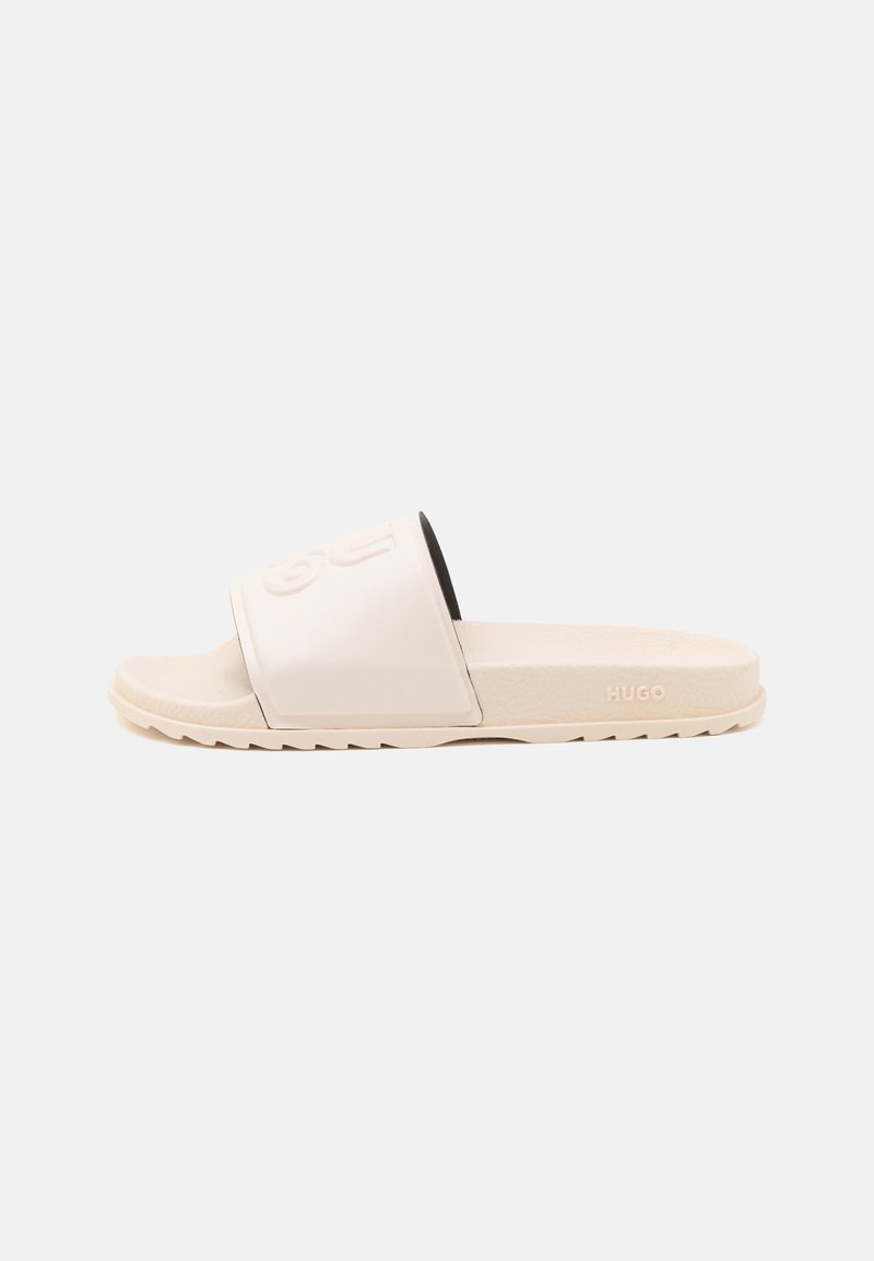 Hvite sandaler med bred stropp som har preget logo. Teksturert såle og glatt fotseng; minimalistisk design med beige detaljer.